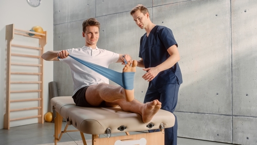 Male patient doing foot mobility exercises with a resistance band in physical therapy